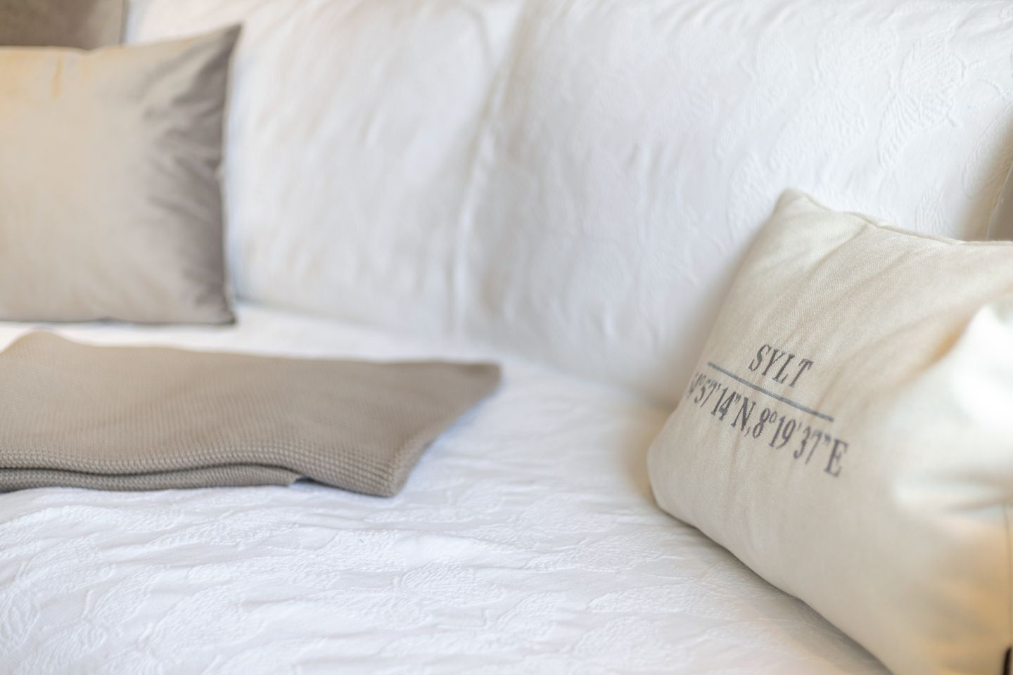 Ein weißes Sofa mit einem beige farbenen Kissen mit Aufschrift.