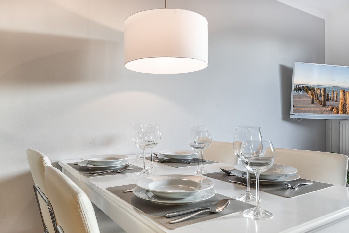 Comedor con una mesa dispuesta para cuatro, una lámpara colgante y un cuadro en la pared.