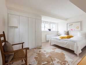A bedroom with a bed, a chair, a cowhide rug, a window with a sailboat, and a framed picture on the wall.