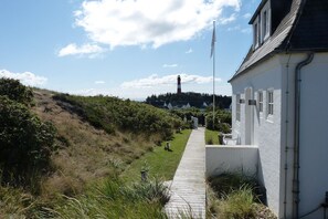 A coastal path leading to a white building with a lighthouse in the distance.