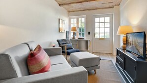 A modern living room with a fireplace, a sofa, a chair, and a television on a cabinet. - Kleine Heimat, Haus Stutenhof Whg. 4 - Die Kleine Heimat Befindet Sich im Herzen von Keitum und (Sylt)