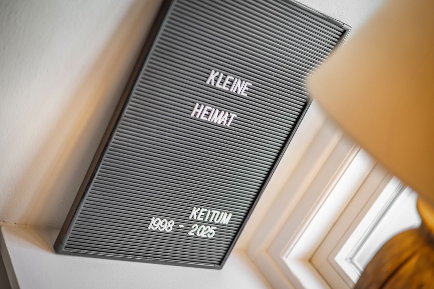 Uma placa com o texto "KLEINE HEIMAT 1998-2025" fixada em uma parede.