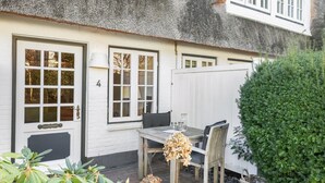 A white cottage with a thatched roof, a wooden table with chairs, and a small garden area with plants and a basket. - Kleine Heimat, Haus Stutenhof Whg. 4 - Die Kleine Heimat Befindet Sich im Herzen von Keitum und (Sylt)