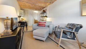 A modern living room with a sofa, armchair, and a small table with a candle. There is a TV and a lamp on a stand. - Kleine Heimat, Haus Stutenhof Whg. 4 - Die Kleine Heimat Befindet Sich im Herzen von Keitum und (Sylt)