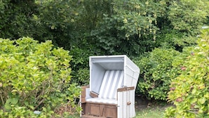 Ein Korbstuhl mit gestreifter Sitzkissen in einem Garten.