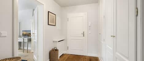 A hallway with white walls, wooden flooring, a framed picture, a basket, and a door.