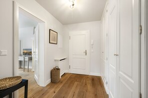 A hallway with white walls, wooden flooring, a framed picture, a basket, and a door.