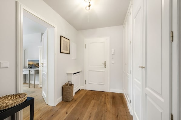 A hallway with white walls, wooden flooring, a framed picture, a basket, and a door.