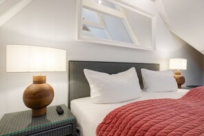 A hotel room with a bed, two bedside tables, a lamp, a remote control, and a window.