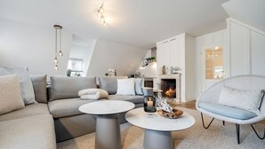 Ein modernes Wohnzimmer mit einer Couch, zwei Couchtischen, einem Korbstuhl, einem Kamin und einer Treppe, die zu einer oberen Ebene führt.