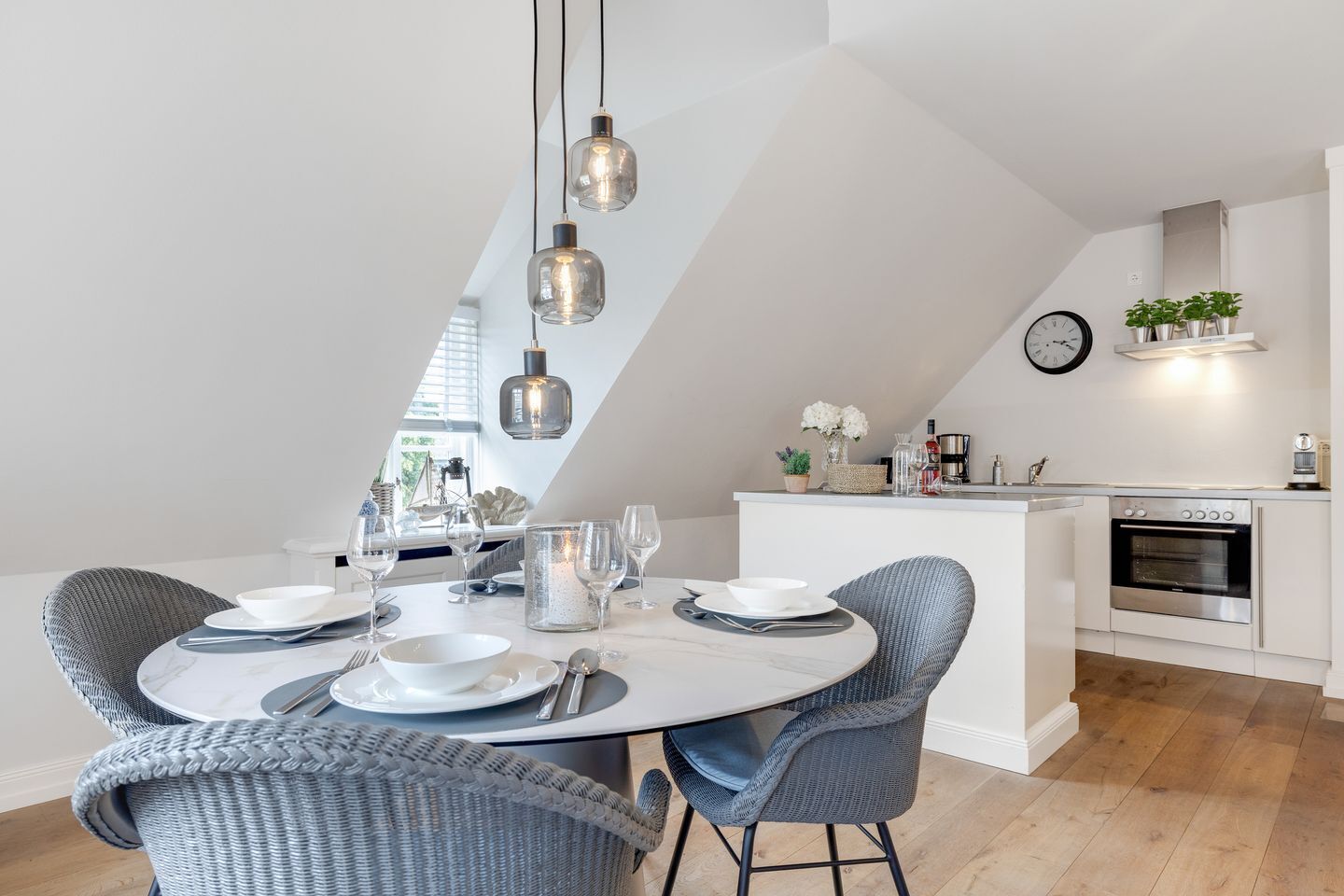 A modern kitchen with a dining area, featuring a round table with chairs, pendant lights, and a built-in oven.