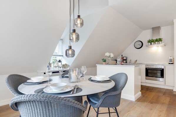 A modern kitchen with a dining area, featuring a round table with chairs, pendant lights, and a built-in oven.