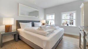 Ein Hotelzimmer mit einem großen Bett, Nachttischlampen, einem Spiegel und einem Fenster mit Blick ins Grüne.