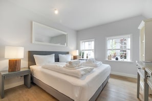 A hotel room with a large bed, bedside lamps, a mirror, and a window with a view of greenery.
