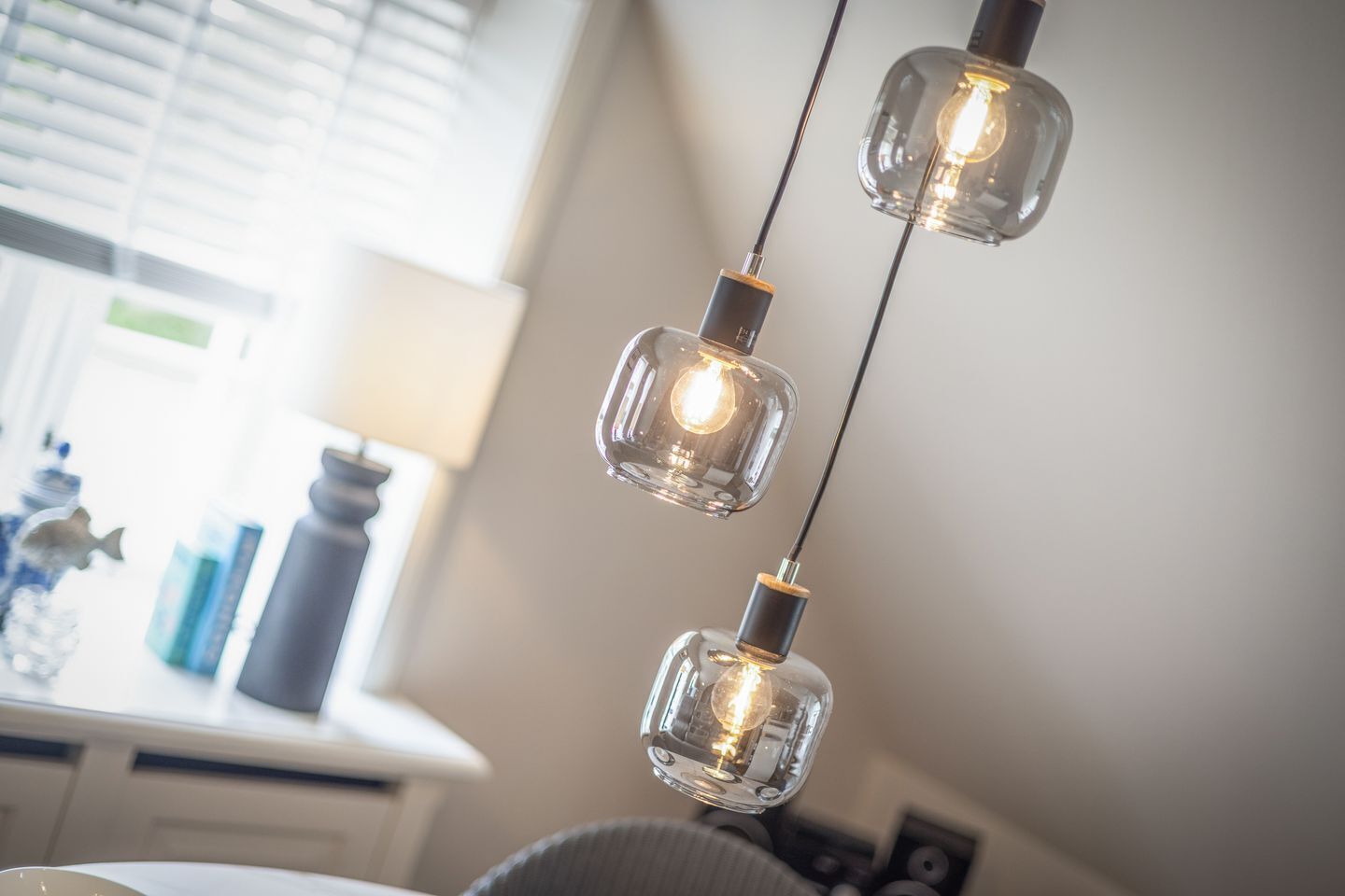 Ein Zimmer mit Schreibtisch, Lampe und einer Pendelleuchte mit drei Glühbirnen.