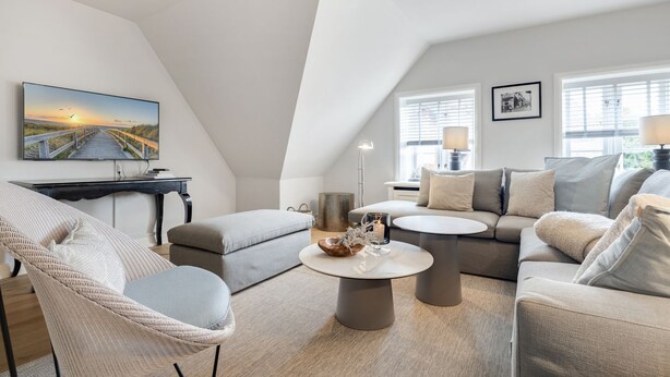 Ein modernes Wohnzimmer mit hohen Decken, einem großen Fernseher und einer gemütlichen Sitzecke mit Sofa und Sesseln.