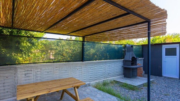 An outdoor patio with a wooden table and benches, a barbecue grill, and a covered area with a bamboo roof. - Villa Azalea 1 in Ortaca (Ortaca)