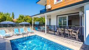A swimming pool with lounge chairs and umbrellas, a covered patio with tables and chairs, and a building with wooden siding and a balcony. - Villa Azalea 1 in Ortaca (Ortaca)