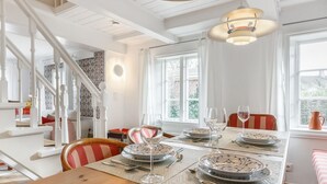 A dining area with a wooden table set for four, white walls, and a staircase in the background.