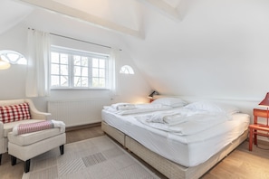 A bedroom with a large bed, a small sofa, a window with curtains, and a lamp. - Gookis Hüs - Gookis Hüs - Idyllisches Friesenhaus in Keitum (Sylt-Ost)