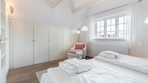 A bedroom with two beds, a chair, a wardrobe, and a window with curtains.