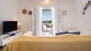 Ein Schlafzimmer mit Bett, Fernseher und Meerblick durch eine offene Tür.