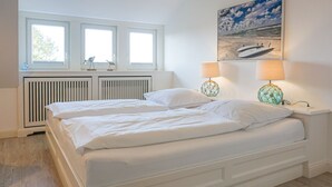 A bedroom with two beds, a radiator, and a beach-themed painting.