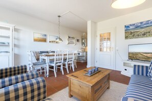 A cozy living room with a dining area, a TV, and a kitchen in the background. - Seestern _ Archsum - Umringt von Salzwiesen und Deichblick Ruht der "seestern" (Sylt)
