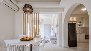 Une cuisine moderne avec des meubles blancs, un réfrigérateur noir et un coin repas comprenant des chaises et une table, le tout dans des tons blancs.