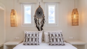 Une chambre avec un lit, deux tables de chevet, un attrape-rêves suspendu et deux fenêtres.