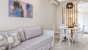 Un salon moderne comprenant un canapé, une table à manger avec des chaises, un luminaire suspendu et un climatiseur fixé au mur.