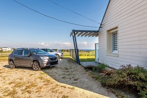 A house with a gravel driveway, a wooden pergola, and two parked cars.