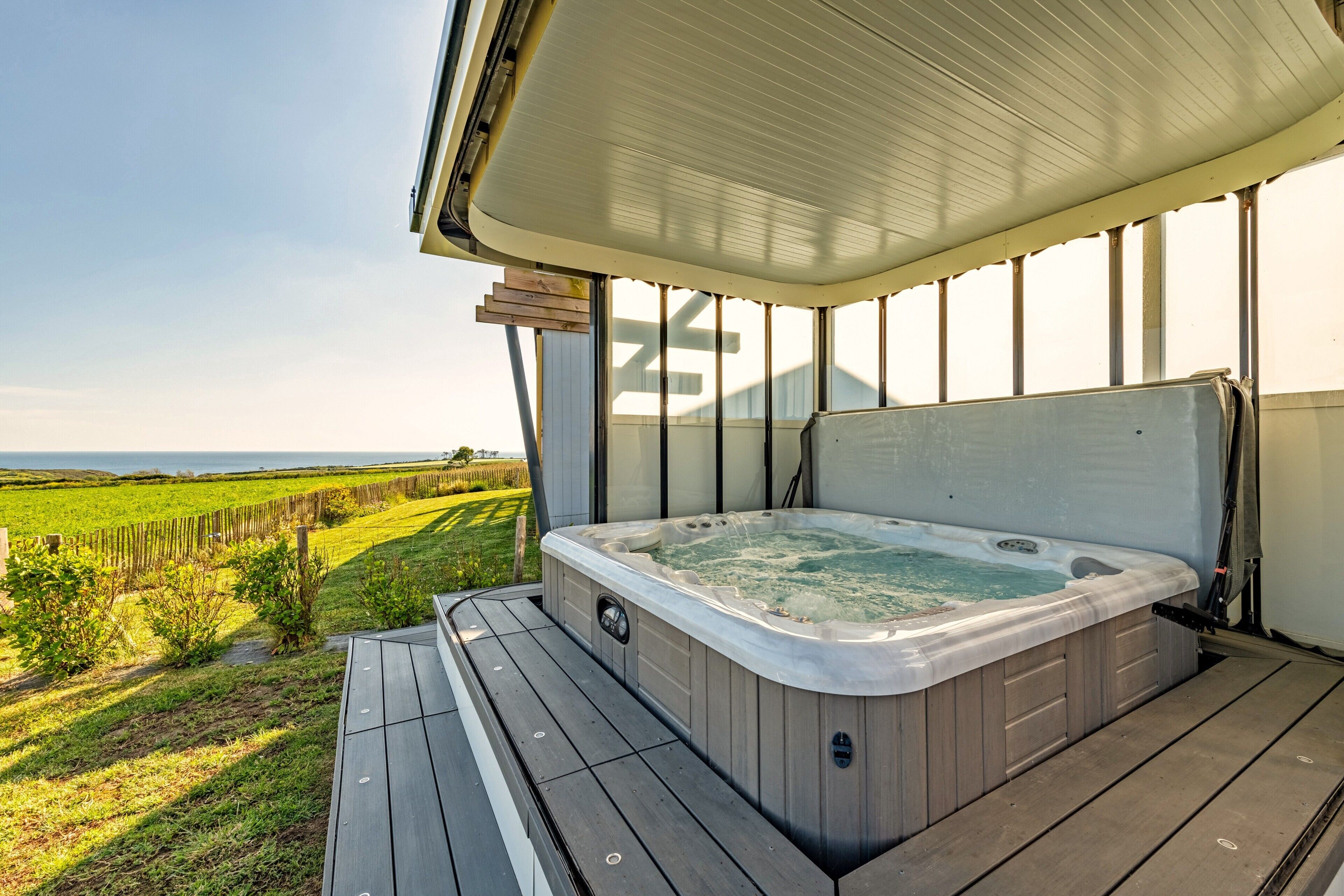 A hot tub on a wooden deck with a view of a green field.
