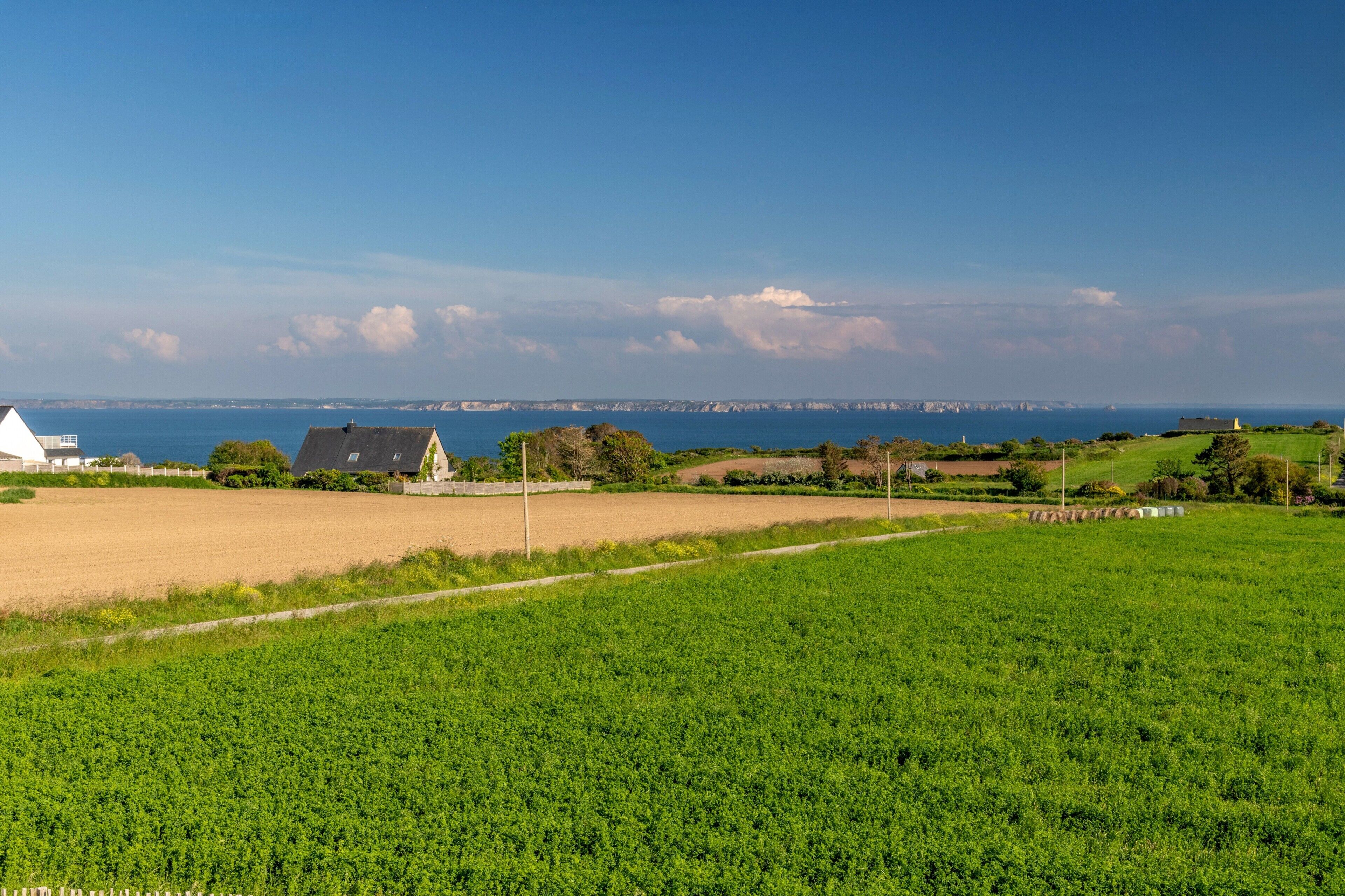 Un paysage rural avec des champs, un bâtiment blanc et une côte lointaine.