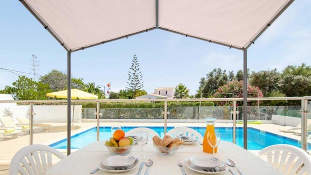 A table set for breakfast with fruit, bread, and juice, overlooking a pool. - Villa Sol Nascente in Porches (Silves)