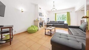A living room with a sofa, a coffee table, a green bean bag, a fireplace, and a television. - Villa Sol Nascente in Porches (Silves)