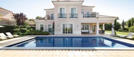 A two-story house with a swimming pool, outdoor seating, and a well-maintained garden.