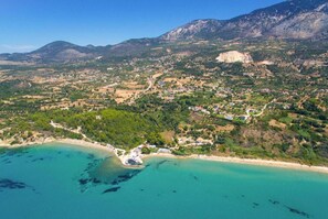 An aerial view of a coastal town with a beach, houses, and mountains in the background.