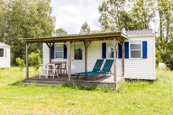 A small house with a porch, a table with chairs, and two lounge chairs.