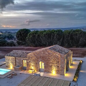 A stone building with a swimming pool, outdoor seating, and a view of the landscape. - Palmento San Lorenzo 6 Emma Villas (Noto)