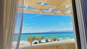 A view through a window with a stone balustrade, overlooking a beach with trees and the sea.