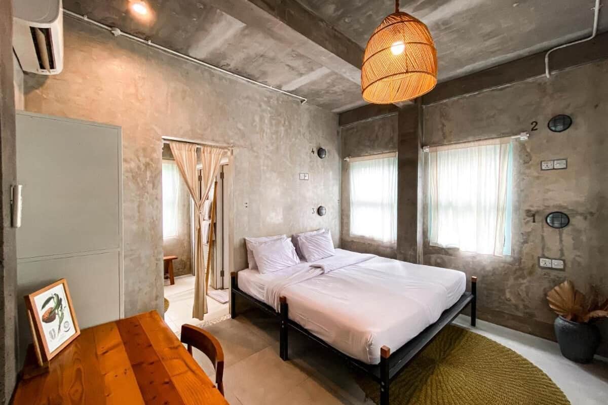 Une chambre à coucher avec un lit, une table en bois, un luminaire suspendu et une fenêtre avec des rideaux.
