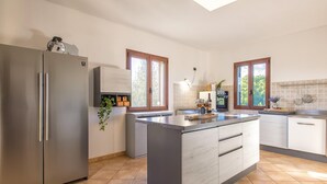 Une cuisine moderne dotée d’un îlot central, d’appareils électroménagers en acier inoxydable et de grandes fenêtres qui laissent entrer la lumière naturelle.
