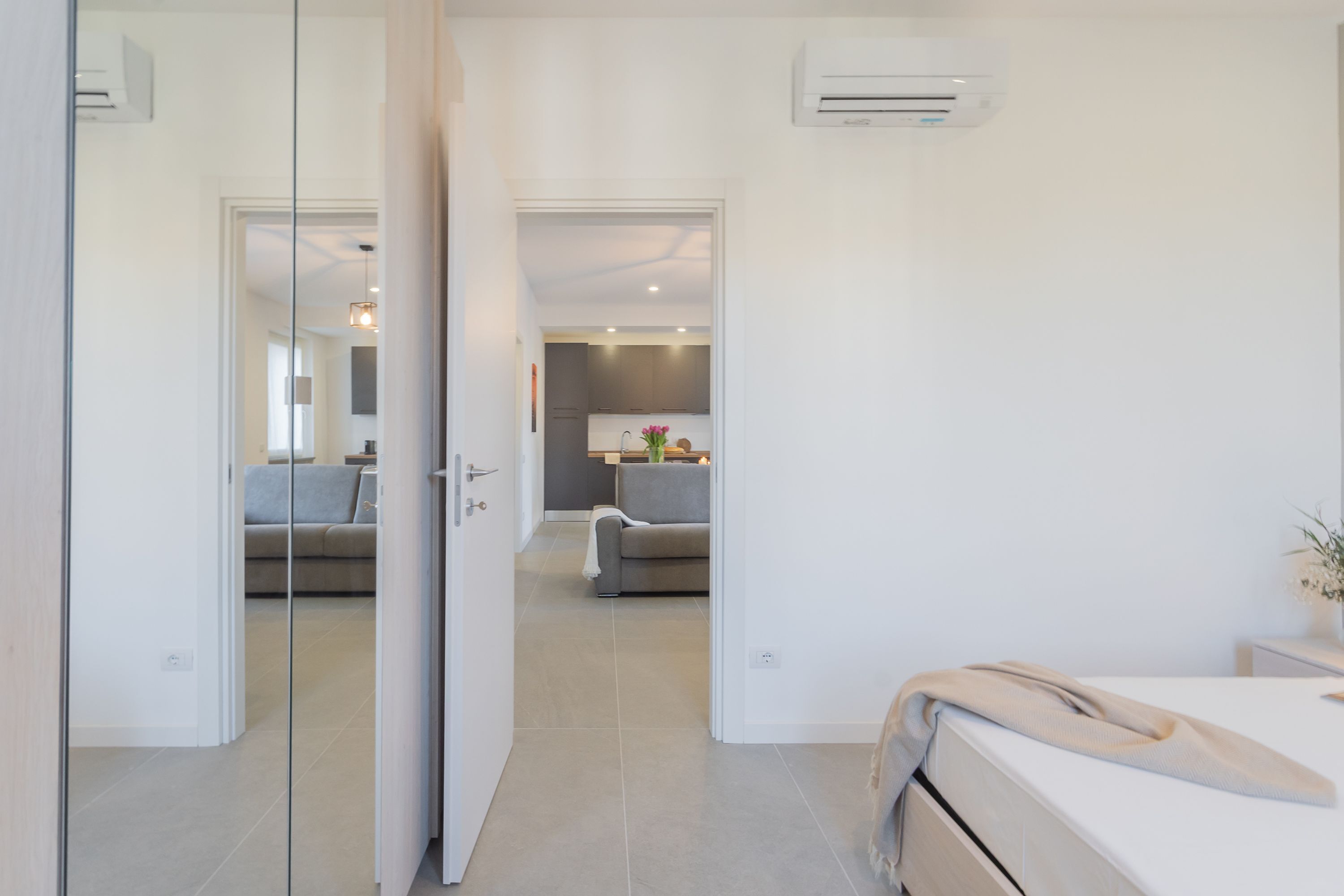 A modern hotel room with a bed, a bedside table, and a view into the adjacent living area.