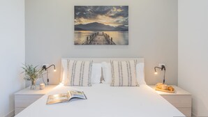 Una cama bien hecha con una revista, un florero con plantas y una bandeja con una taza y un croissant en una mesita de noche.