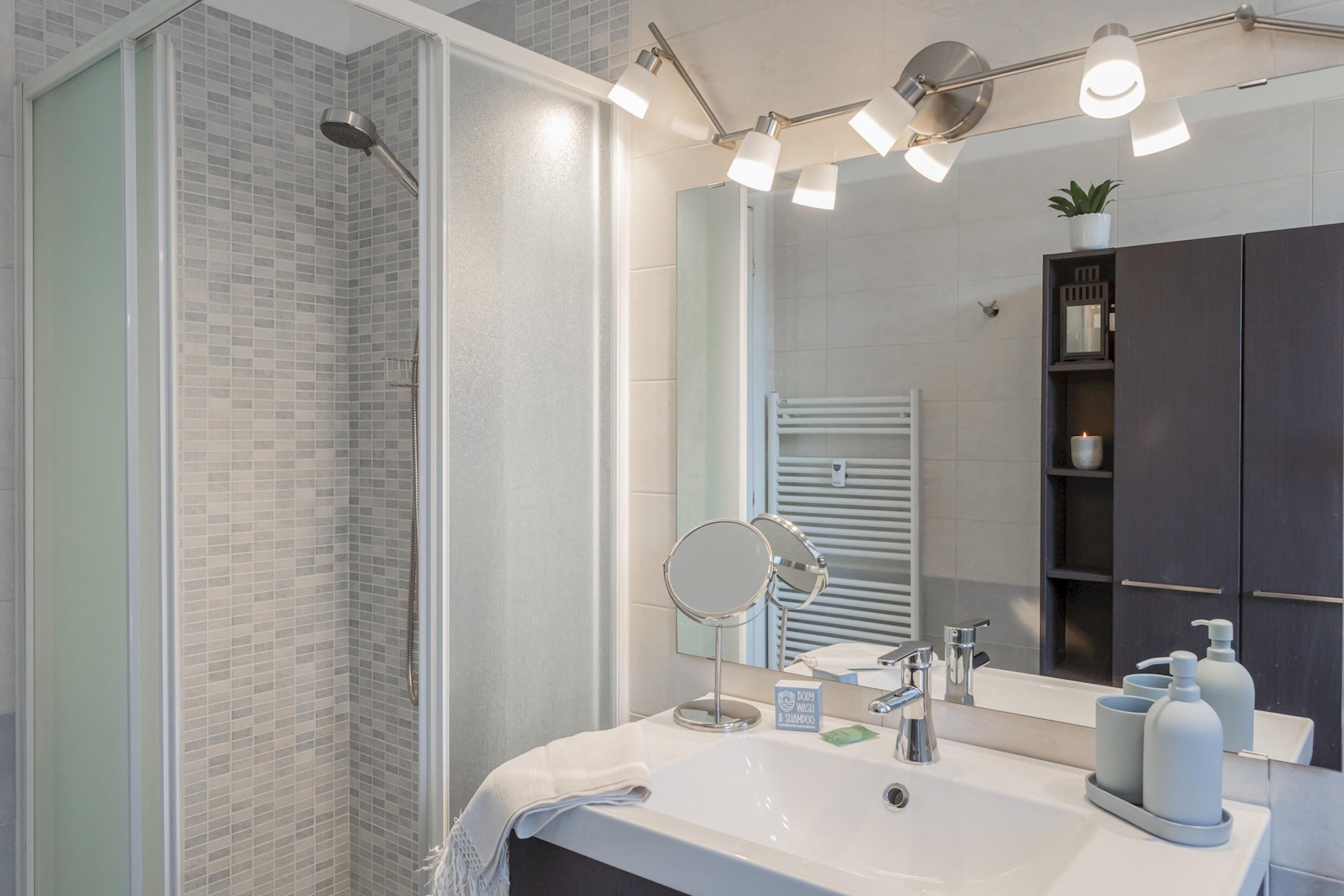 A modern bathroom with a glass-enclosed shower, a large mirror, and a vanity with a sink and toiletries.