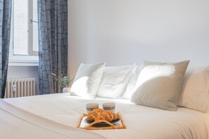 A neatly made bed with white linens, two pillows, and a tray with croissants and two cups. - Chiara s Apartment (Como)