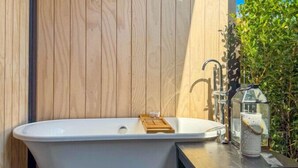 A freestanding bathtub in a wooden deck area with a table and a lantern. - Stunning Matakana Retreat! (Matakana)