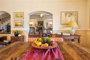 Een eetruimte met een houten tafel, een fruitmand als decoratie, een trap en uitzicht op de keuken.
