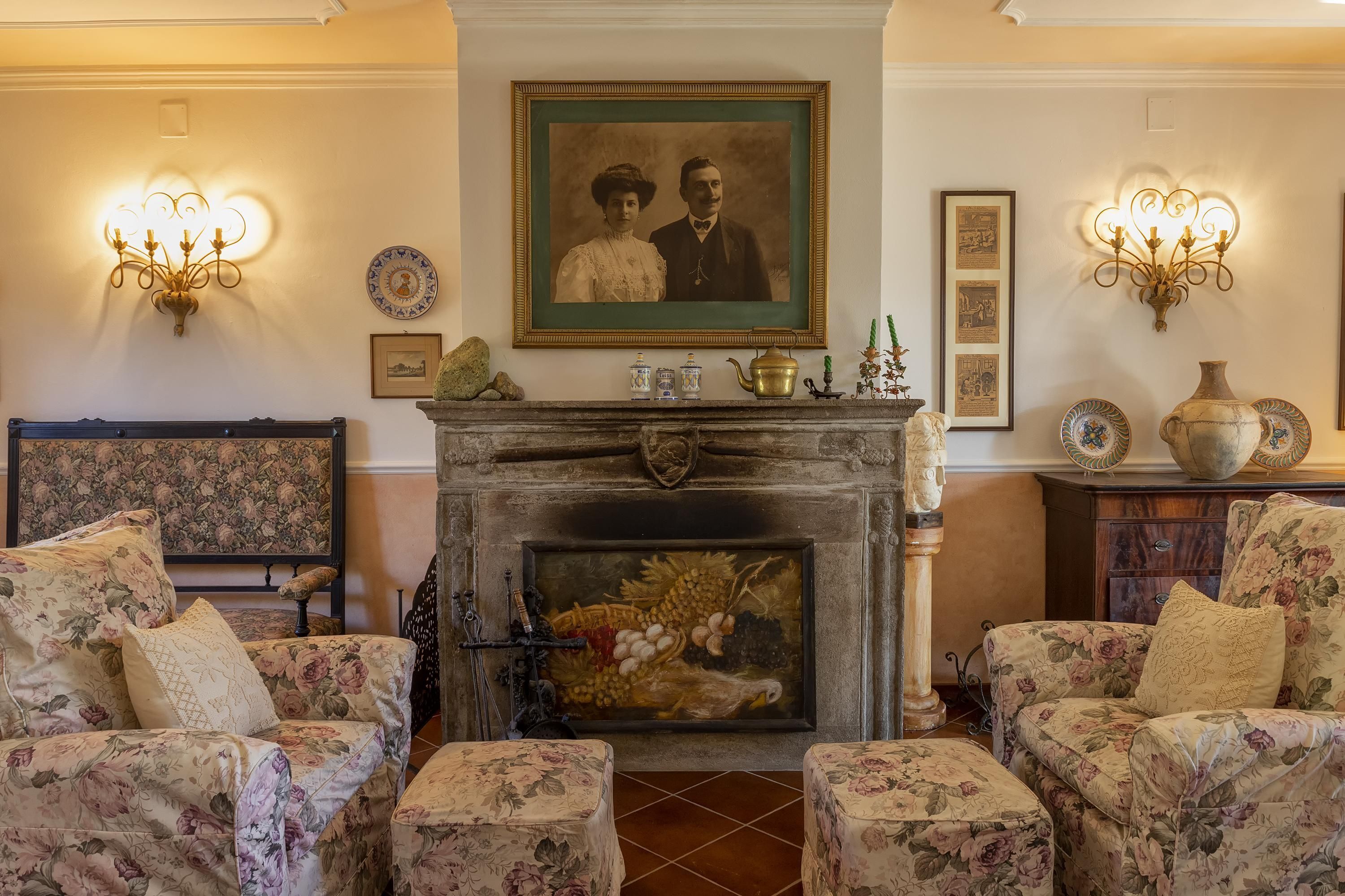 A traditional living room with floral upholstery, a fireplace, and wall-mounted sconces.